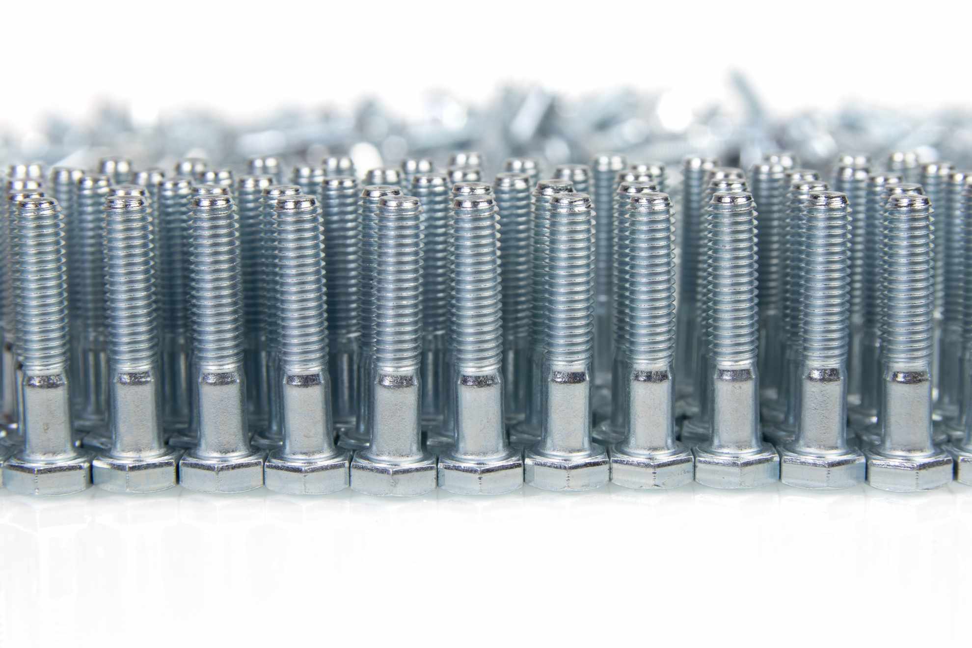 Bild: Frisch produzierte Schrauben stehen auf dem Kopf in Reihen auf einem Fließband, weißer Hintergrund